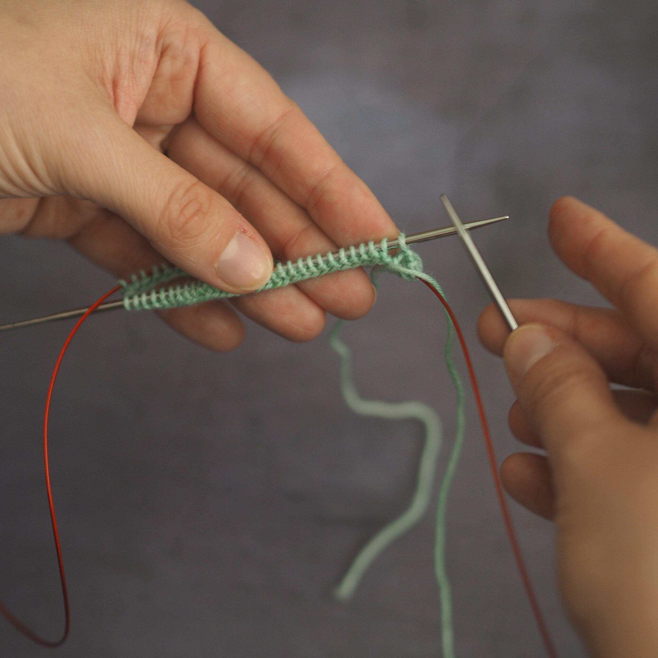 hands holding mint yarn on magic loop needles