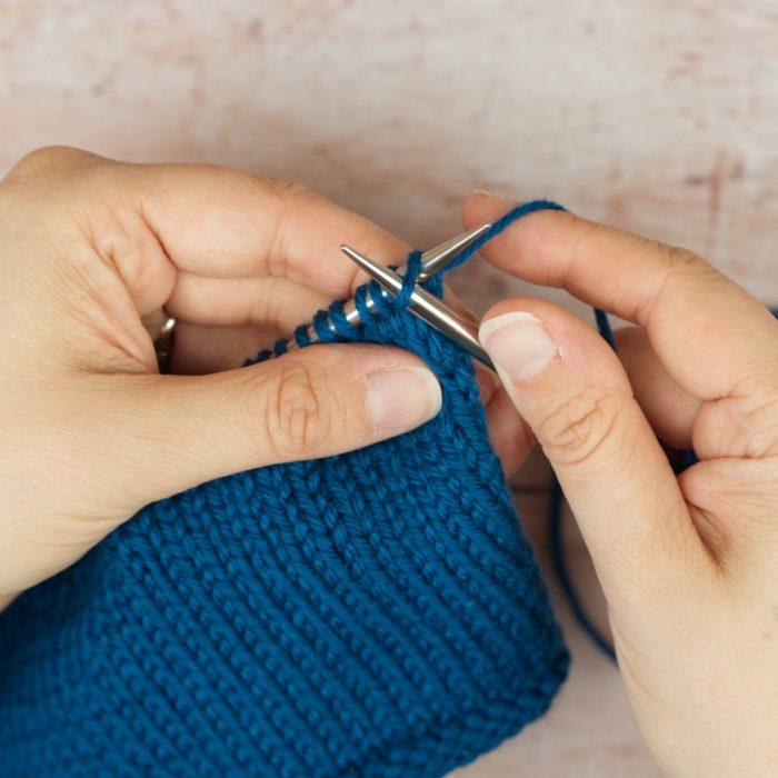 hands hold blue knitting and needle inserted purlwise