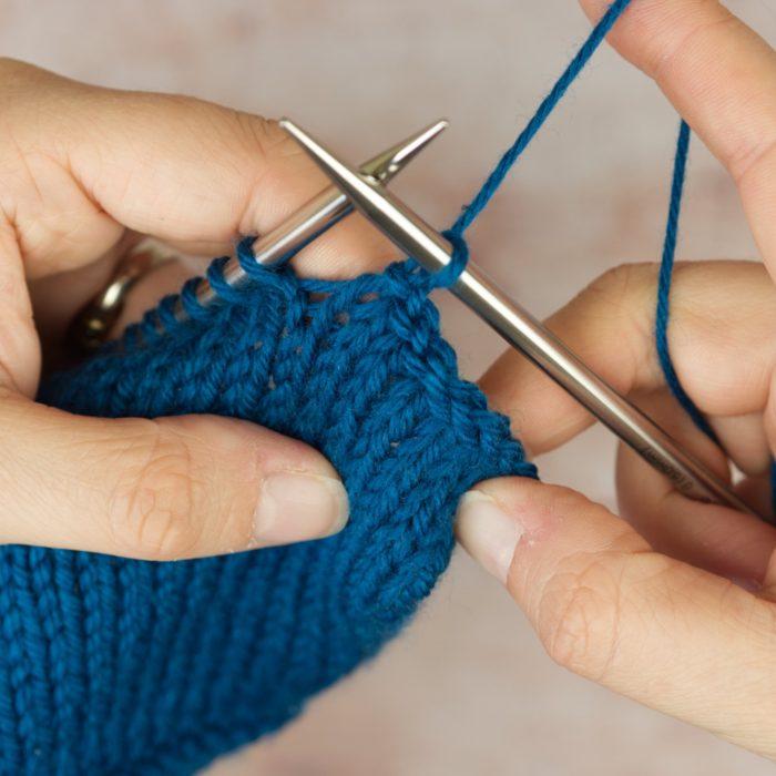 hands hold blue knitting showing an icelandic bind off