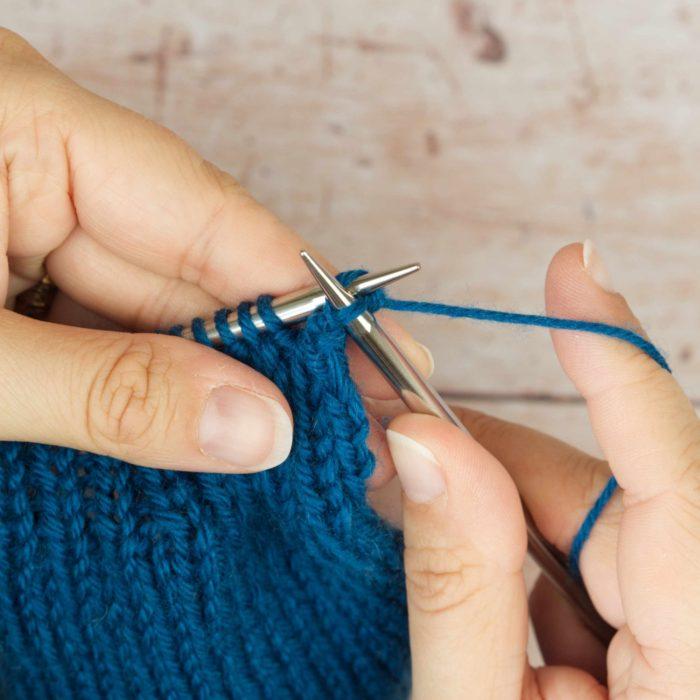 hands holding mid blue knitting casting off a stitch