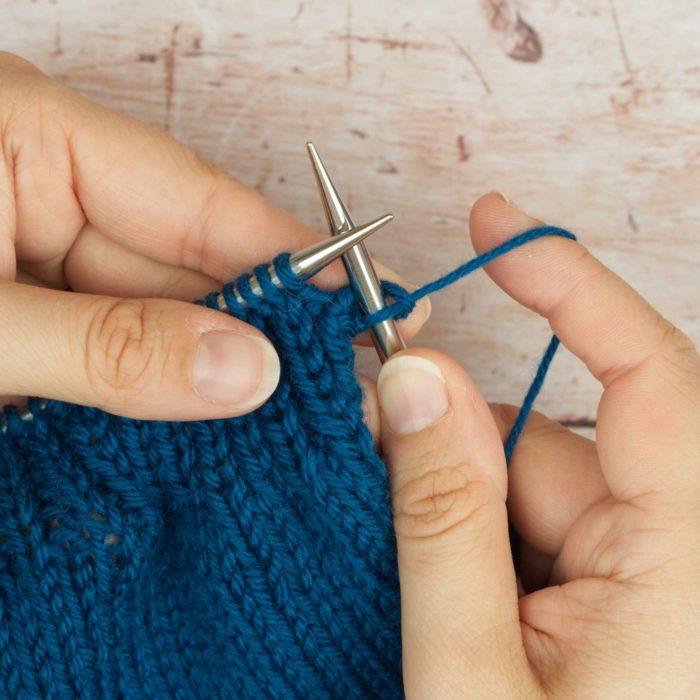 hands holding mid blue knitting