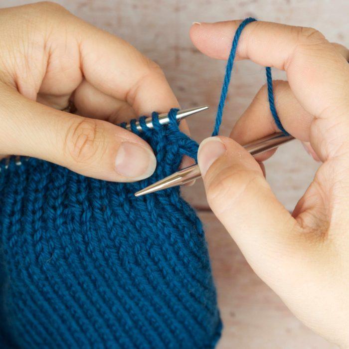 hands holding mid blue knitting rotating forward
