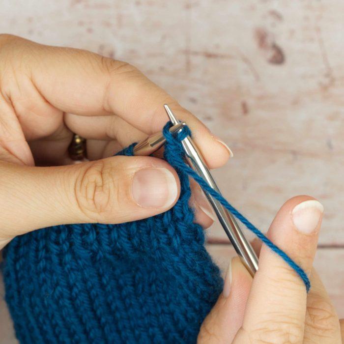 hands holding mid blue knitting casting off a stitch