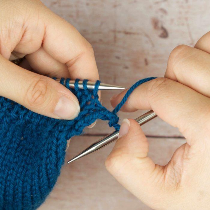 hands holding mid blue knitting and right needle rotating forward