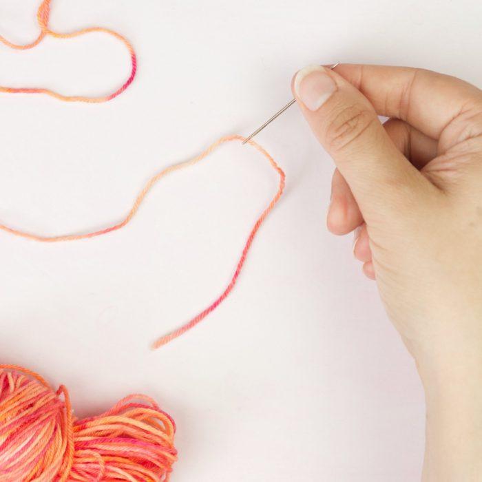 hands holding yarn yarn and a threaded needle