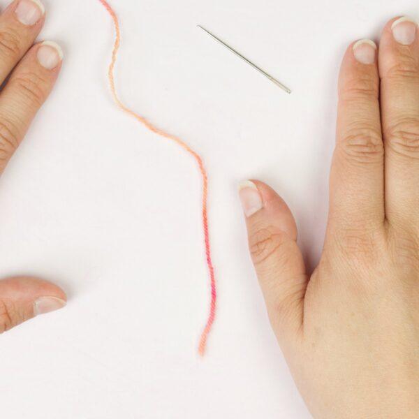 hands holding yarn yarn and a threading a needle