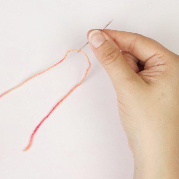 hands holding yarn yarn and a threaded needle