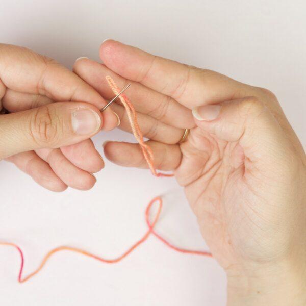 hands holding yarn yarn and a threaded needle