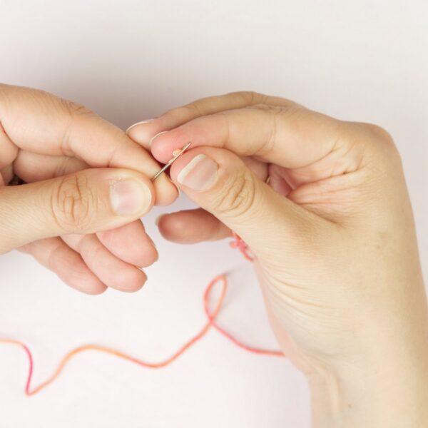 hands holding yarn yarn and a threading a needle