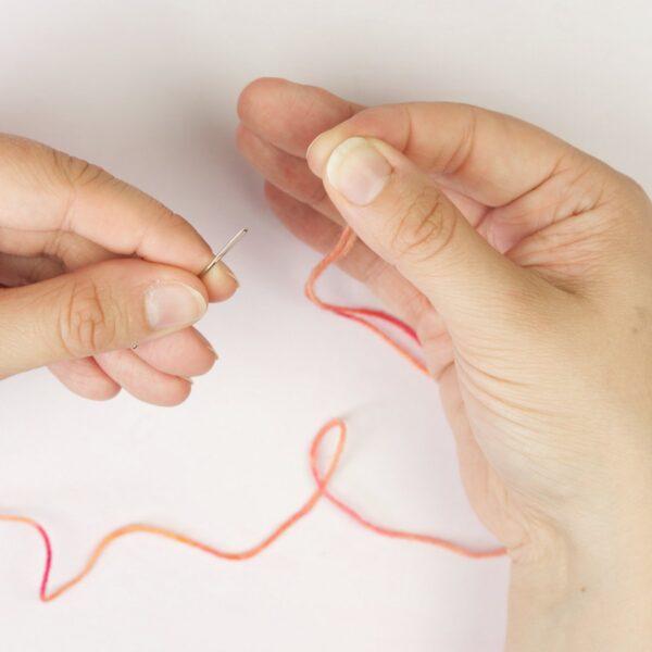 hands holding yarn yarn and a threading a needle
