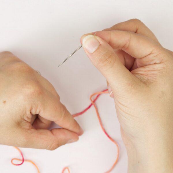 hands holding yarn yarn and a threading a needle